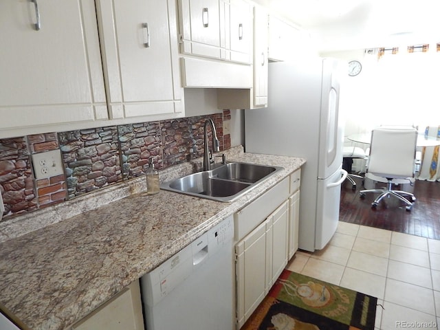 kitchen featuring light tile patterned floors, white appliances, a sink, white cabinets, and decorative backsplash