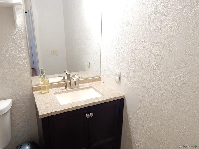 half bath featuring toilet, a textured wall, and vanity