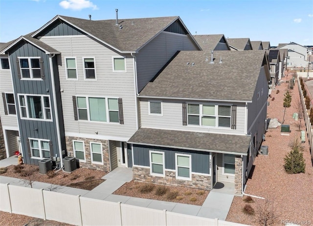 townhome / multi-family property with board and batten siding, stone siding, central AC, and a shingled roof