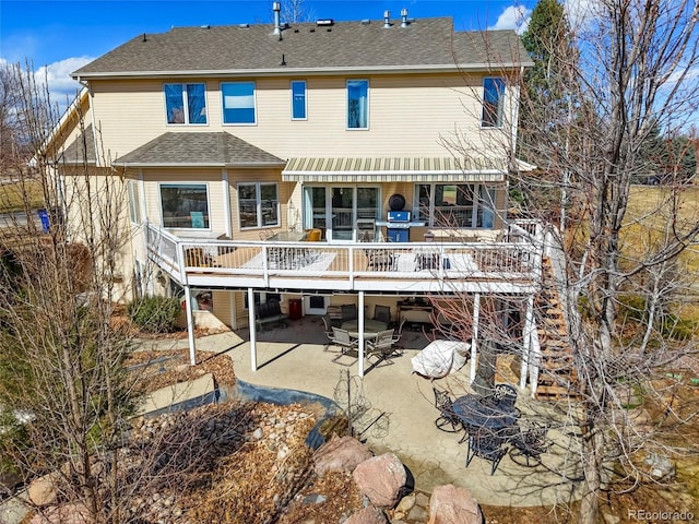 rear view of house with a deck, a patio, and roof with shingles