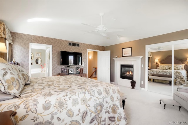 carpeted bedroom featuring visible vents, connected bathroom, wallpapered walls, ceiling fan, and a glass covered fireplace