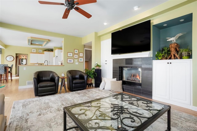 living area with baseboards, a fireplace, wood finished floors, and a ceiling fan