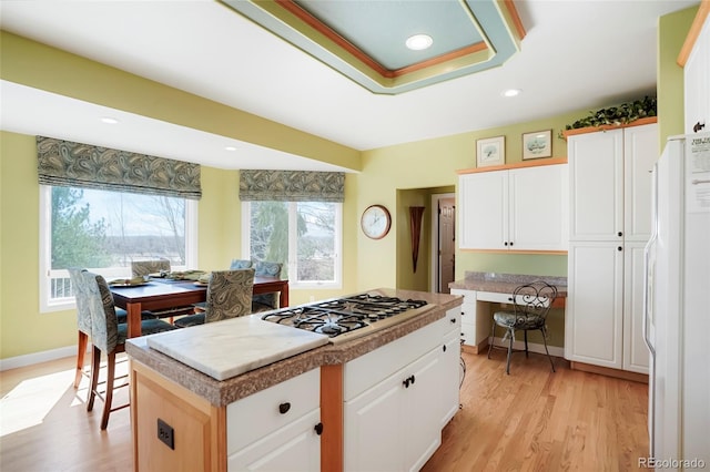 kitchen featuring a kitchen island, baseboards, light wood-style flooring, freestanding refrigerator, and gas stovetop