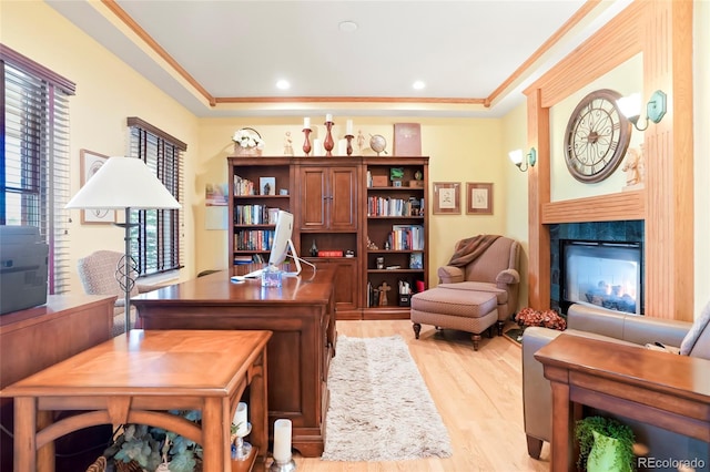 office area with a raised ceiling, light wood-style flooring, a high end fireplace, and ornamental molding