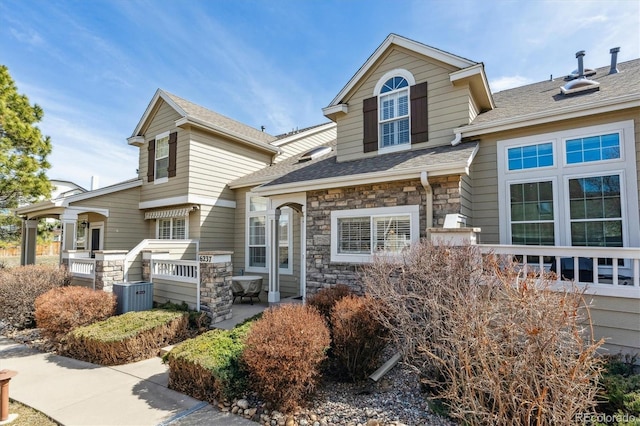 view of front of house featuring stone siding, central AC unit, and a shingled roof