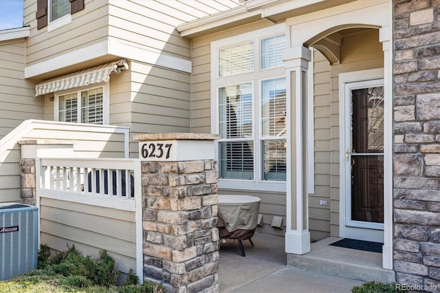 view of exterior entry featuring central air condition unit and stone siding