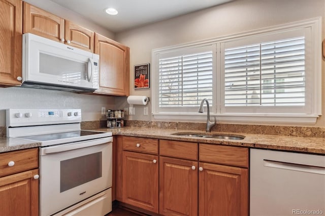 kitchen featuring light stone countertops, recessed lighting, brown cabinets, white appliances, and a sink