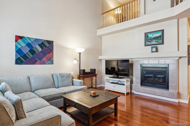 living room featuring baseboards, a high ceiling, wood finished floors, and a tiled fireplace