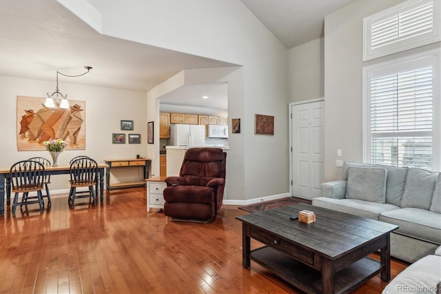 living room featuring baseboards, high vaulted ceiling, an inviting chandelier, and hardwood / wood-style flooring