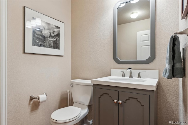 bathroom with vanity, toilet, and a textured wall