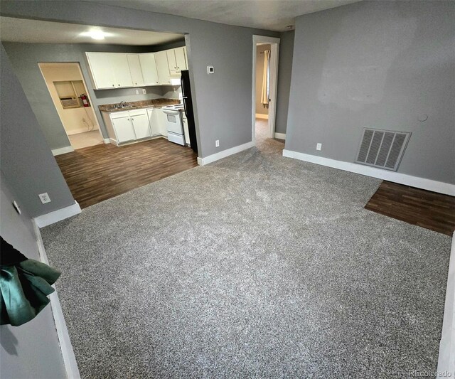 520 Prairie Rd, Colorado Springs, CO 80909 - unfurnished living room with baseboards, dark carpet, dark wood-style flooring, and a sink