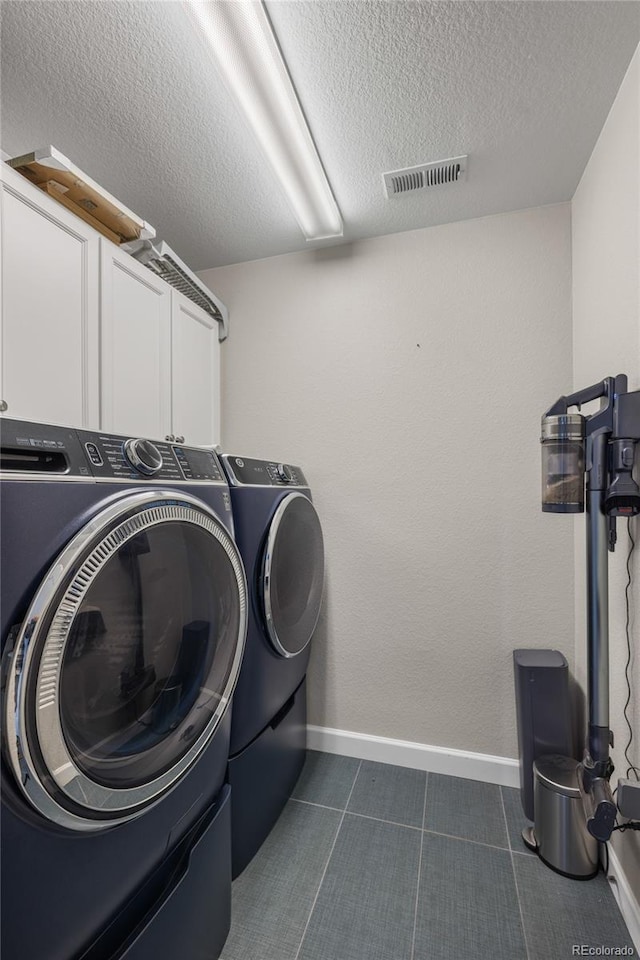 washroom featuring a textured ceiling, cabinets, and washing machine and clothes dryer