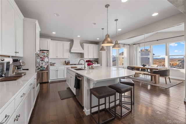 kitchen with a kitchen island with sink, custom range hood, and white cabinetry