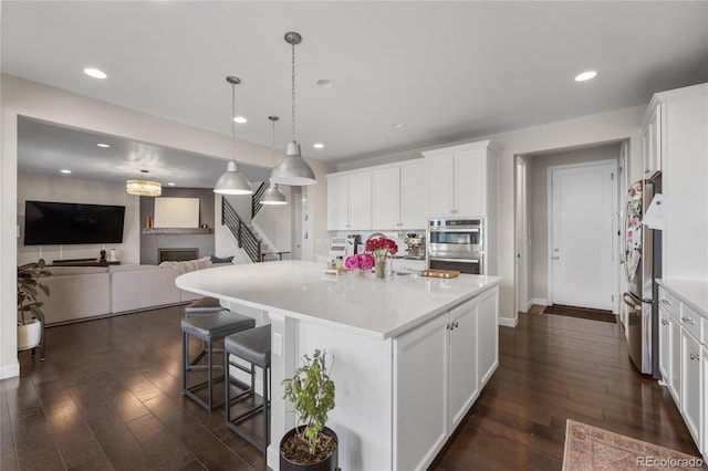 kitchen with hanging light fixtures, an island with sink, stainless steel appliances, dark wood-type flooring, and white cabinets