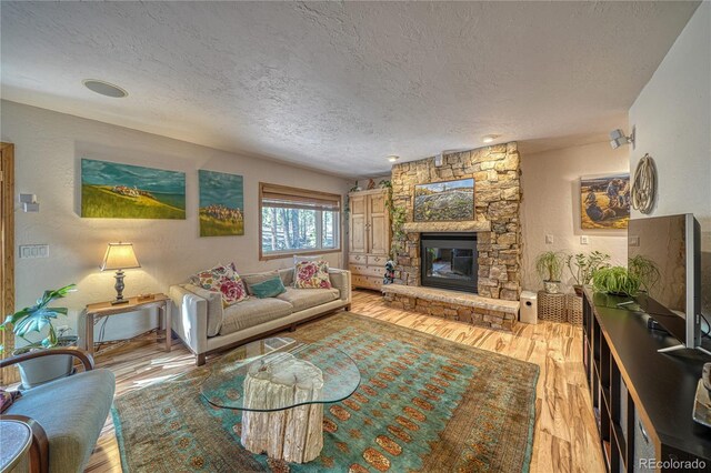 living room featuring a stone fireplace, light wood-type flooring, and a textured ceiling