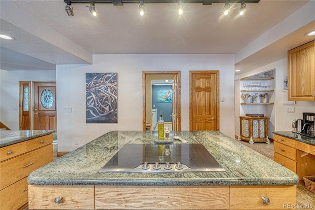 kitchen featuring a kitchen island, black electric cooktop, rail lighting, and dark stone counters