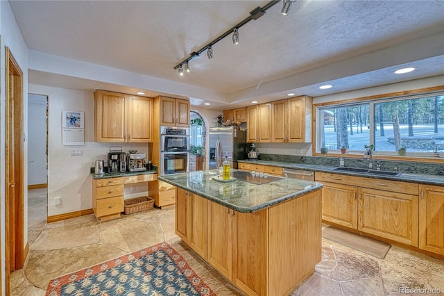 kitchen featuring rail lighting, a textured ceiling, stainless steel appliances, sink, and a center island