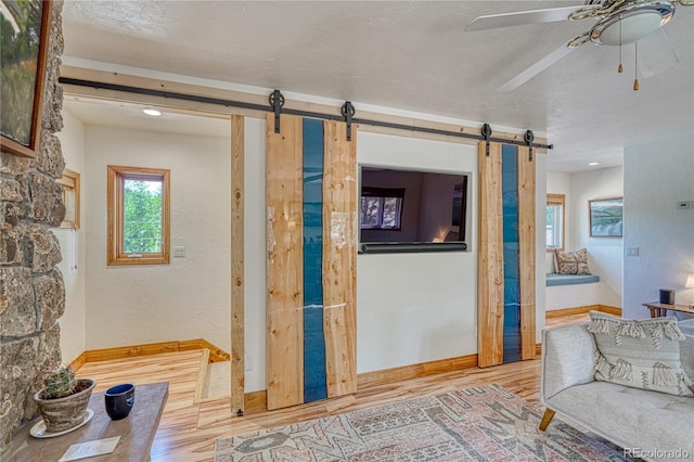 living room with a barn door, ceiling fan, hardwood / wood-style floors, and a textured ceiling