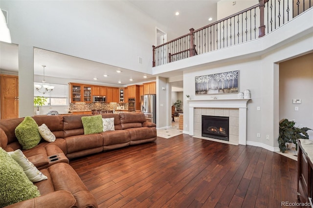 living room featuring dark wood-type flooring, a tile fireplace, a high ceiling, and a notable chandelier