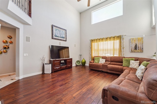 living area featuring a towering ceiling, baseboards, wood finished floors, and a ceiling fan