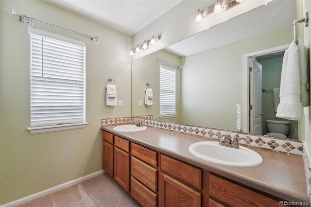 full bathroom featuring double vanity, toilet, baseboards, and a sink