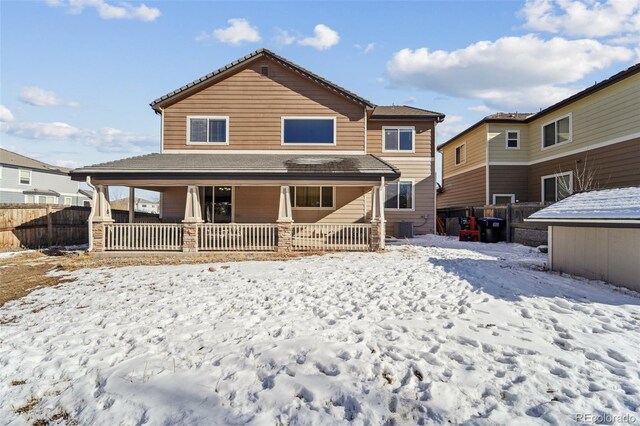 snow covered house featuring central AC unit, a porch, and fence