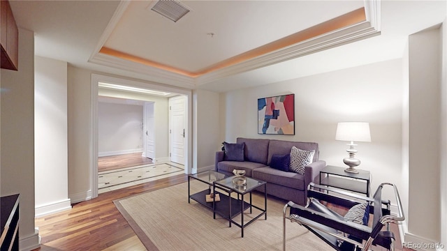 living room with a tray ceiling, wood-type flooring, and ornamental molding