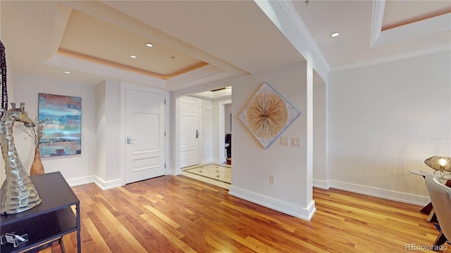 entryway with a raised ceiling, crown molding, and light hardwood / wood-style flooring