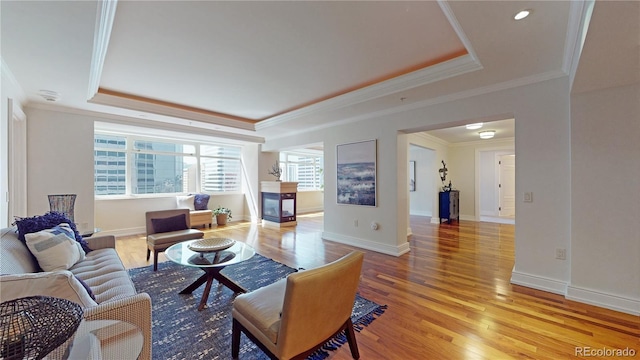 living room featuring a multi sided fireplace, wood-type flooring, a tray ceiling, and ornamental molding