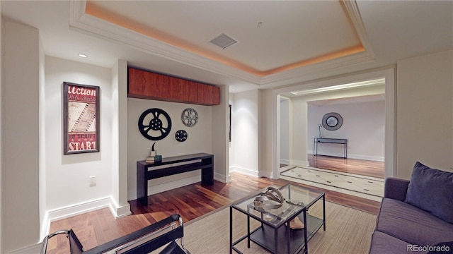 living room featuring wood-type flooring, a raised ceiling, and ornamental molding