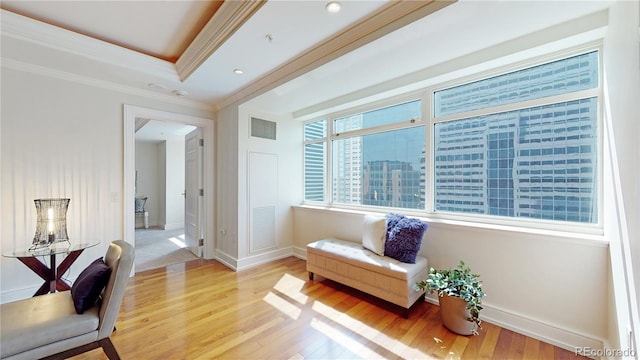 living area featuring light wood-type flooring, crown molding, and a tray ceiling