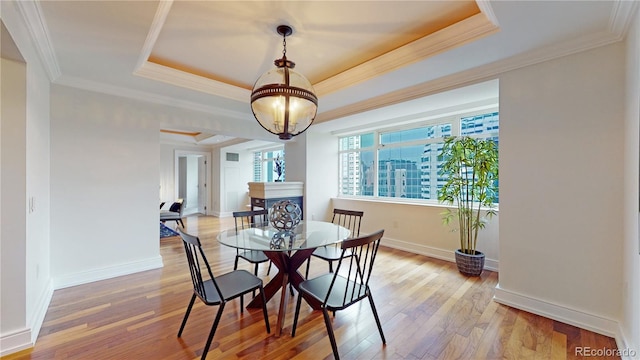 dining area with a chandelier, hardwood / wood-style flooring, a raised ceiling, and crown molding