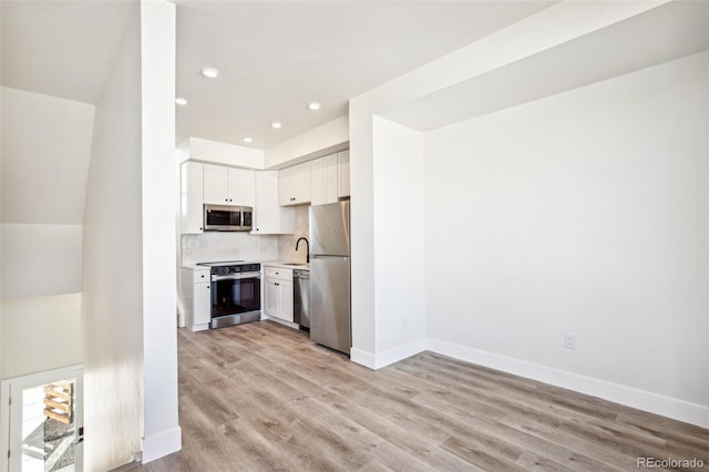 kitchen featuring light wood finished floors, tasteful backsplash, appliances with stainless steel finishes, white cabinets, and baseboards