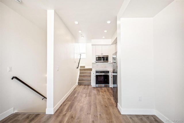 kitchen featuring tasteful backsplash, baseboards, appliances with stainless steel finishes, light wood-type flooring, and white cabinetry