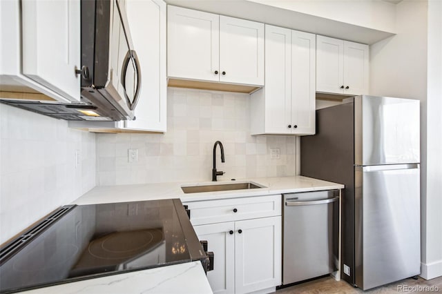 kitchen featuring appliances with stainless steel finishes, a sink, white cabinetry, and light stone countertops