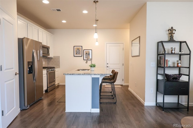 kitchen featuring sink, hanging light fixtures, stainless steel appliances, white cabinets, and a center island with sink