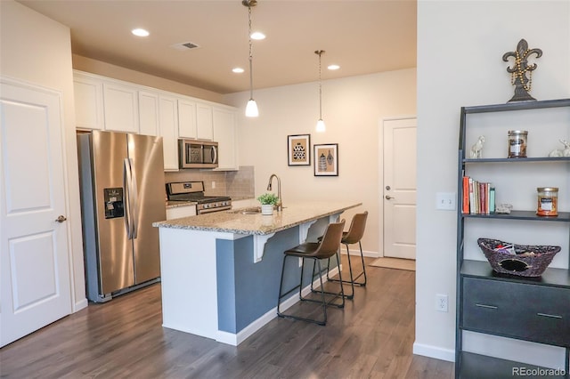 kitchen featuring appliances with stainless steel finishes, an island with sink, hanging light fixtures, and white cabinets