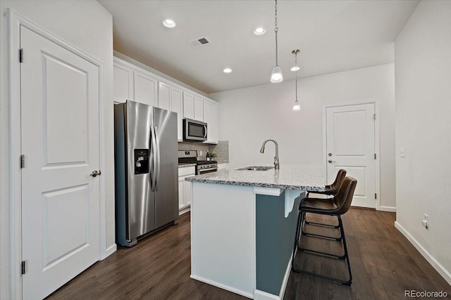 kitchen featuring hanging light fixtures, stainless steel appliances, white cabinets, and a center island with sink