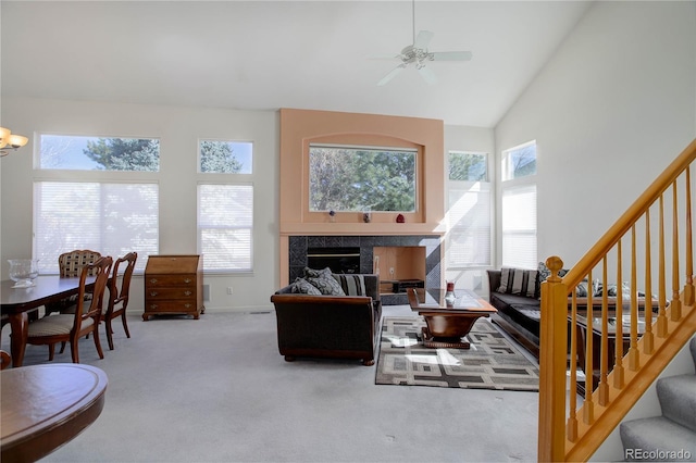 carpeted living area with baseboards, ceiling fan, stairway, a fireplace, and high vaulted ceiling