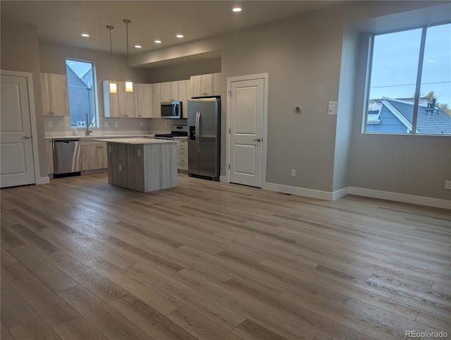 kitchen featuring stainless steel appliances, pendant lighting, a kitchen island, and light hardwood / wood-style flooring