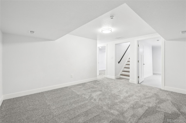 finished basement with a textured ceiling, stairs, baseboards, and carpet flooring