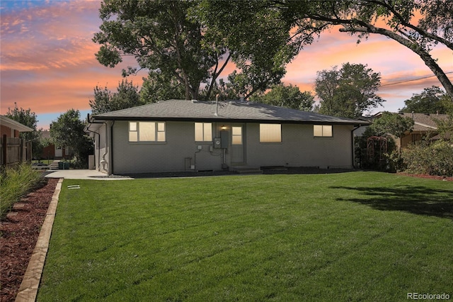 back of house featuring brick siding, a lawn, and fence