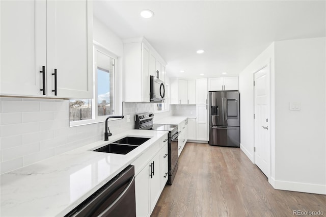 kitchen featuring stainless steel appliances, a sink, white cabinets, backsplash, and light stone countertops