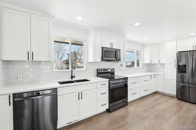 kitchen with stainless steel appliances, light countertops, white cabinetry, a sink, and wood finished floors