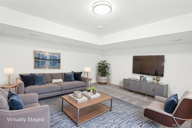 carpeted living room featuring a tray ceiling, visible vents, and baseboards