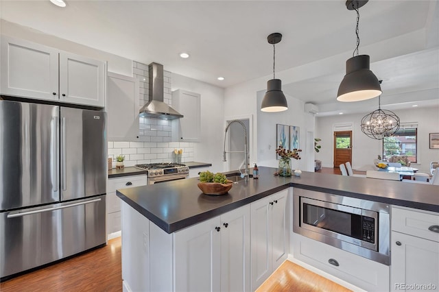 kitchen with stainless steel appliances, light hardwood / wood-style flooring, hanging light fixtures, and wall chimney range hood