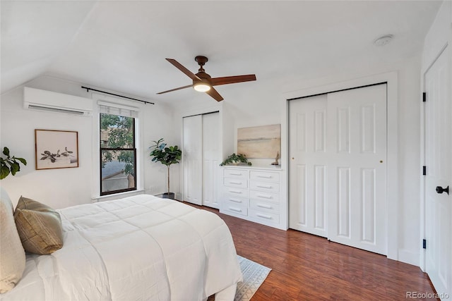 bedroom with ceiling fan, wood-type flooring, two closets, and a wall mounted air conditioner