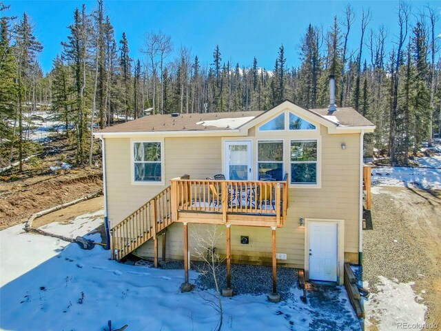 snow covered rear of property featuring stairway, a wooded view, and a wooden deck