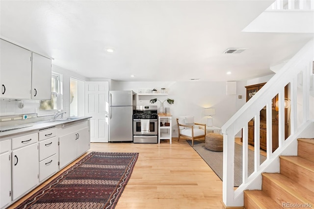 kitchen featuring white cabinetry, sink, tasteful backsplash, light hardwood / wood-style floors, and appliances with stainless steel finishes