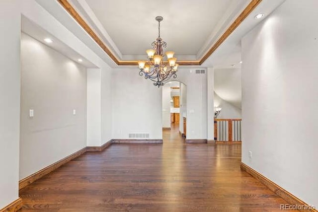 empty room featuring dark hardwood / wood-style flooring, a notable chandelier, ornamental molding, and a raised ceiling